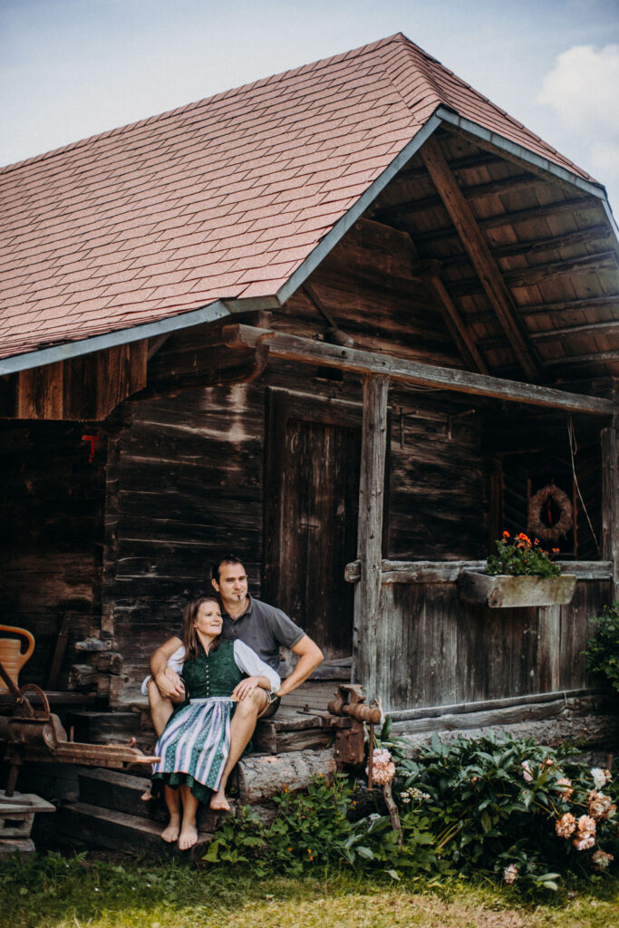 Bäuerin und Bauer sitzen vor traditionellem Holzhaus – Biohof Pamer, Breitenau